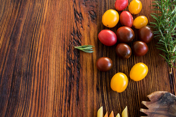 bunte kleine tomaten mit rosmarin und holzlöffel auf einer rustikalen holzplatte
