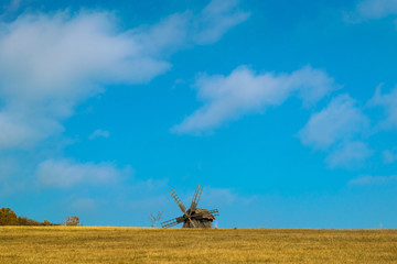 Fototapeta premium Old wooden windmill in the field. Windmill in the yellow field with dried grass against a blue sky