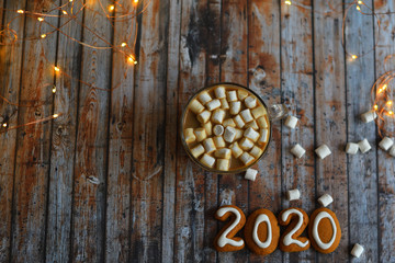 Number 2020 from gingerbread cookies.cocoa, marshmallows, homemade cookies and heart made from coffee beans on wooden background with bokeh New Year's lights.