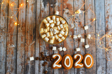 Number 2020 from gingerbread cookies.cocoa, marshmallows, homemade cookies and heart made from coffee beans on wooden background with bokeh New Year's lights.