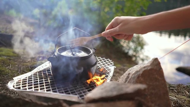 Tee koffee kettle on a disposable grill open fire with moka pot on the shore of a forest lake. Coffee pot close-up
