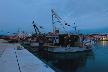 Fototapeta premium Koper, Slovenia-September 27, 2019: Scenic evening view of harbor in Koper. Vintage fishing boats moored in harbor. Beautiful autumn evening. Romantic and peaceful scene