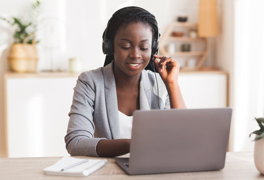 Beautiful female call center operator wearing headset and typing at laptop