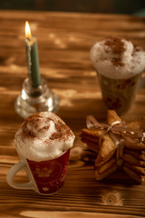 Top view of Christmas creamy hot beverage with gingerbread cookies and a burning candle on wooden background