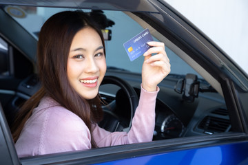 Happy beautiful Asian woman sitting inside new car blue and showing credit card pay for oil, pay a tire, maintenance on the garage, Make payment for refueling car on gas station, Automotive financing