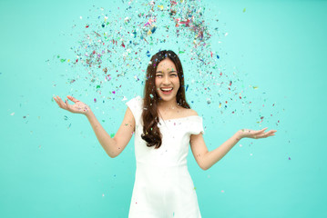 Cheerful young Asian woman celebrating with colorful confetti isolated on green background, Thai...