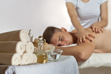 Obraz na płótnie Canvas Blonde in t-shirt doing a massage to the guy. The towels are stacked in the foreground. Man lying on the table on a white background.
