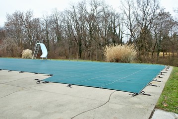 backyard swimming pool with diving board and pool slide tarped up and closed down for winter