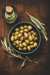 Flat-lay of fresh harvested seasonal pickled green Mediterranean olives in bowl and olive oil in...
