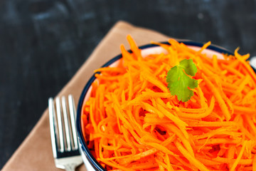 Korean carrot salad. Raw chopped carrots with sauce in white bowl.