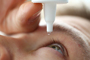 Male hand putting liquid drops in his eye solving vision problem