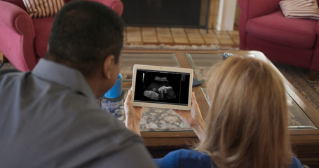 African American and Caucasian couple looking at ultrasound of grandchild