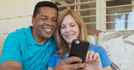 Close up of happy older couple sitting on porch and using smartphone together