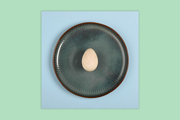 One turkey egg on colored paper background. Food concept in minimal style. Top view. Alternative decoration.
