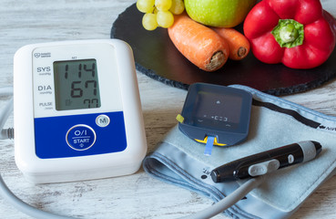 Devices for measuring blood pressure and blood glucose on a table with fruit and vegetables