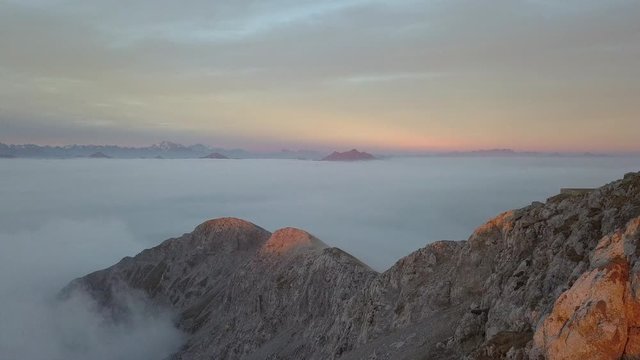 Aerial drone backward flight footage over the Central Italian Alps and a carpet of clouds at sunset time.