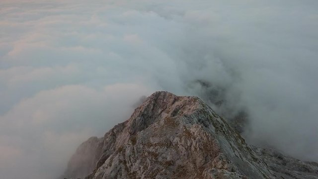 Aerial drone forward flight footage over a ridge of Central Italian Alps and a carpet of clouds at sunset time.