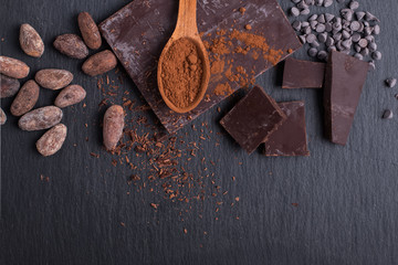 Cocoa beans, powder and chocolate pieces on black slate background