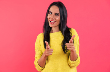 Cool mood. Close-up photo of a self-confident young woman, who is posing in a yellow sweatshirt, smiling and pointing to the camera with finger guns.