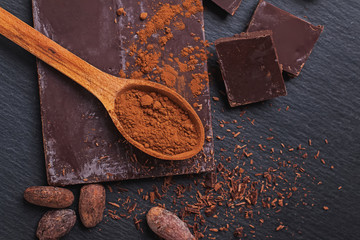 Natural chocolate and cocoa powder in a wooden spoon on black stone bacgkround