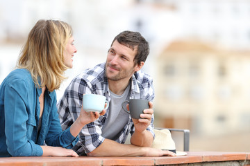Relaxed couple talking holding mugs in a balcony