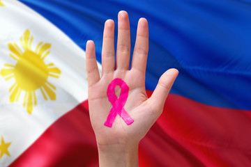 Philippines awareness concept. Close-up awareness ribbon painted on palm on national flag background. October Pink day and world cancer day.