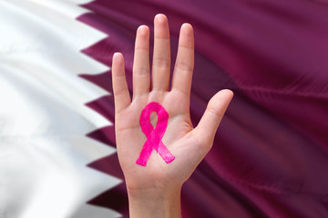 Qatar awareness concept. Close-up awareness ribbon painted on palm on national flag background....