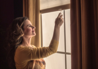 Home blinds window shades woman opening shade blind during sunny morning. Mature woman holding modern cordless top down luxury curtains indoors.