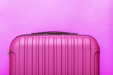 Modern pink suitcase on pink background close up with copy space for text. Minimal style travel...
