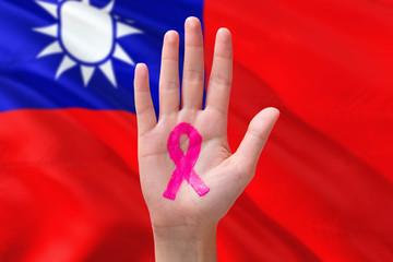 Taiwan awareness concept. Close-up awareness ribbon painted on palm on national flag background. October Pink day and world cancer day.