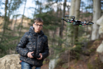 Teen boy controls a drone on a remote control drone in a park