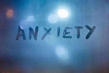 the word anxiety written by finger on night wet glass with blurred classic blue lights in background