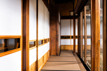 Fototapeta na wymiar Traditional japanese home or ryokan with shoji sliding paper doors tatami mat floor in corridor hallway leading to room by glass windows