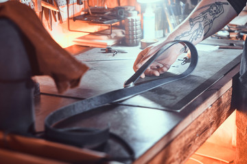 Experienced leather master is working on his new project at the dark workshop.