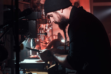 Experienced leather master is working on his new project at the dark workshop.