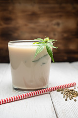 milk from hemp seeds is poured into a glass. Nearby cannabis leaf. Nearby marijuana seeds. wooden background