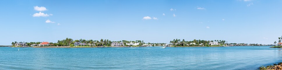 Fototapeta na wymiar Naples, Florida Nelson's Walk houses buildings with water on Dollar bay palm trees, blue sky in residential community vacation homes panorama view