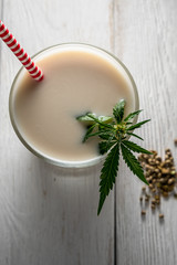 Hemp milk is poured into a glass. On the surface is a cannabis leaf. Nearby marijuana seeds