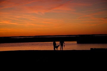 Sunset over Assateague Island over marshes, salt water bay with silhouette of couple walking on the edge