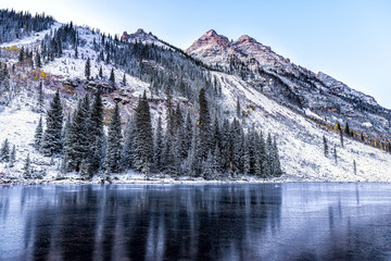 Maroon Bells morning reflection of pine trees in Aspen, Colorado rocky mountain closeup of winter snow frozen lake