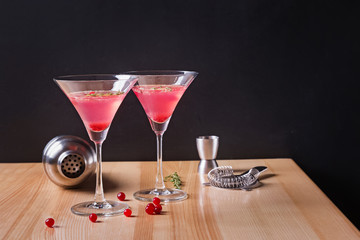 Martini glasses with cranberry cocktail and barmen tools on the wooden table.