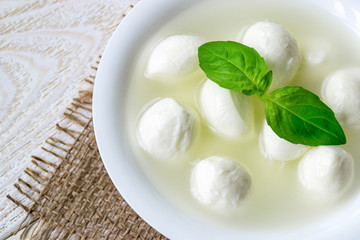 Close-up of bowl with mini mozzarella cheese balls in a brine and basil on a  white rustic wooden...