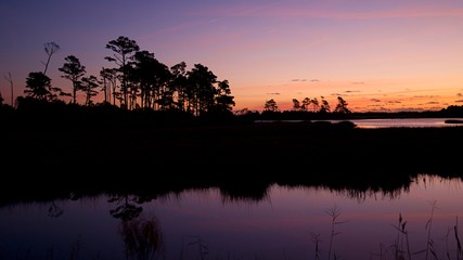 Obraz na płótnie Canvas Sunset over Assateague Island over marshes, salt water bay with silhouette