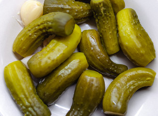 Green pickled cucumbers. Salted cucumbers. Sour pickled small cucumbers. Appetizer on a white plate in a plate. Macro.
