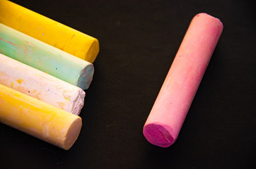 Children`s multicolored crayons on a black background. Chalk for drawing in different angles and different sides. Children's chalk for drawing in macro.