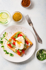 French breakfast concept. Poached egg on toasted bread with cherry tomatoes, cheese and herbs on a boiled background