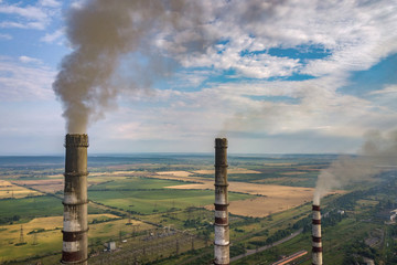 Aerial view of high chimney pipes with grey smoke from coal power plant. Production of electricity with fossil fuel.