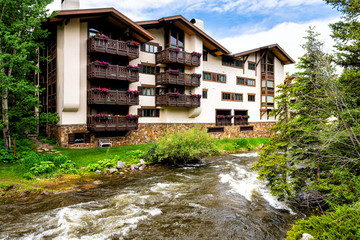 Vail European Swiss style resort town apartment building balcony exterior with flower decorations in Colorado by Gore creek river water flowing - obrazy, fototapety, plakaty