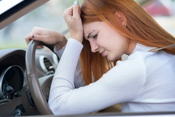 Sad tired yound woman driver sitting behind the car steering wheel in traffic jam.