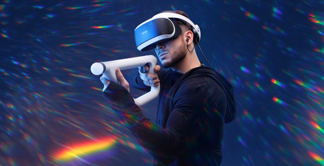 Obraz na płótnie Canvas Beautiful man over dark magic background. Gamer guy in glasses of virtual reality with controllers in hands. Augmented reality, game, hobby concept. VR. Rainbow flares.